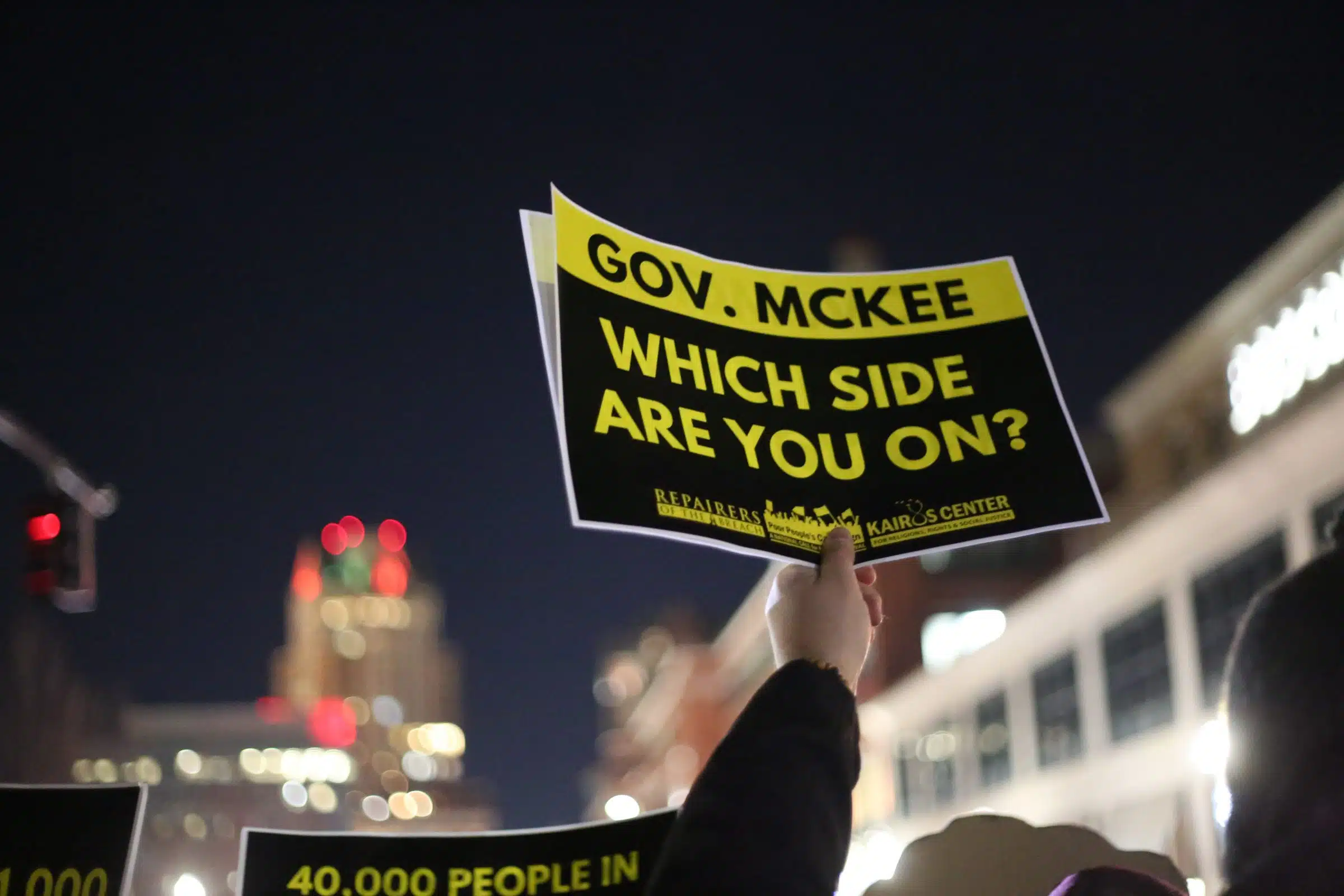 Gov. McKee Which Side are You on? poster held aloft outside the Rhode Island State House in protest against homelessness